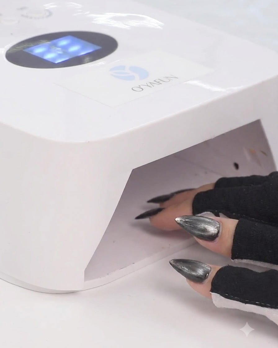 黒い指なし手袋を着けた手が、白いUV/LEDネイルランプの中に指を入れてジェルを硬化させている様子。