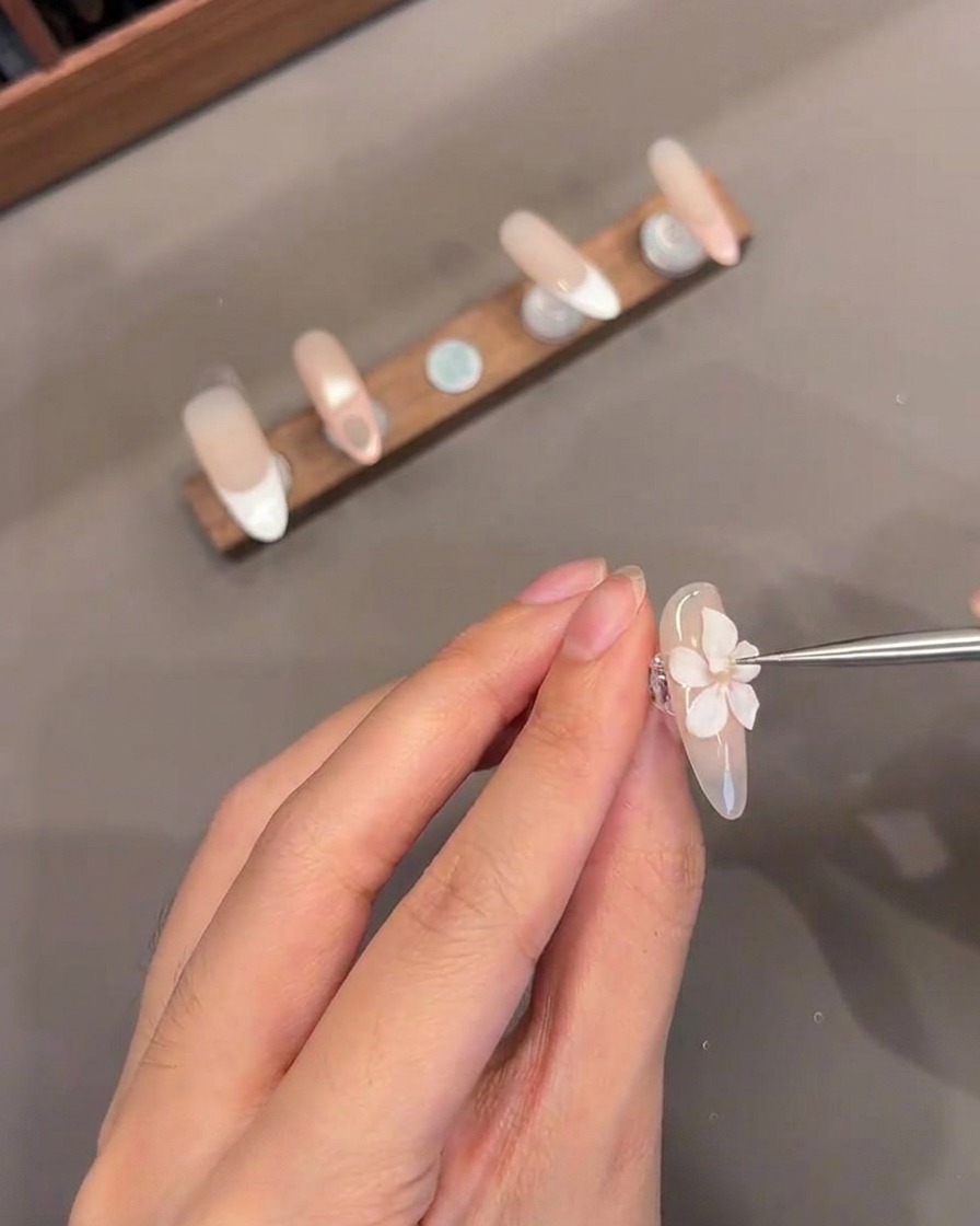 爪の上で造形された3Dフラワーの中心に細いツールが小さな白いジェルの中心を加えているクローズアップ。