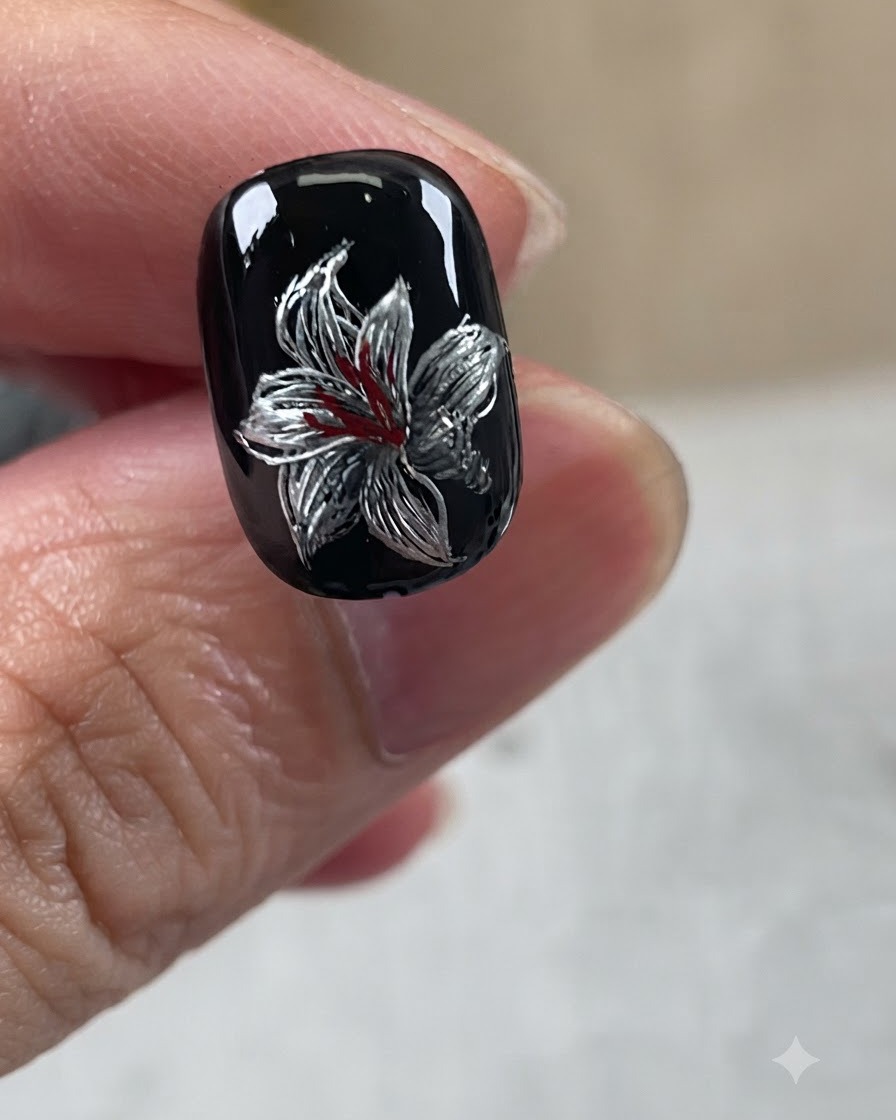 ブラックベース、シルバーの花びら、ホワイトのアクセント、レッドの中心ディテールを特徴とする、完成したメタリックリリーネイルデザイン。