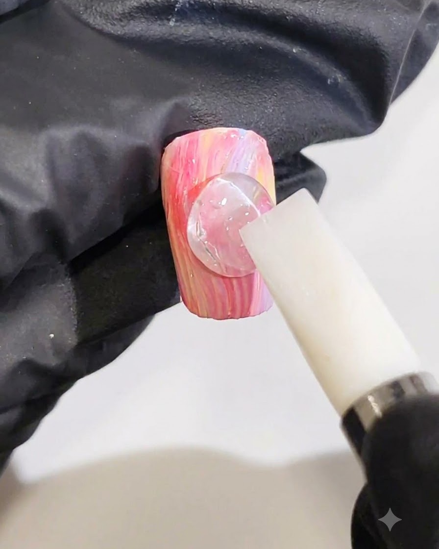 手袋を着用した手が白いシリコンツールを使い、ピンクとイエローのマーブルネイル上でクリアな3Dジェルのドットをリップルラインに成形している様子。