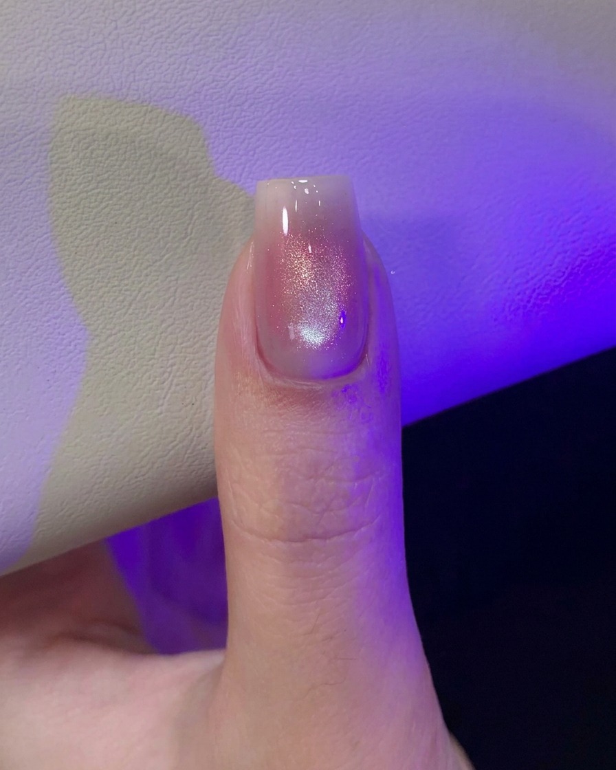 紫色のUV/LEDライトの下で、模様を作った直後のマグネットネイルを硬化させている親指。